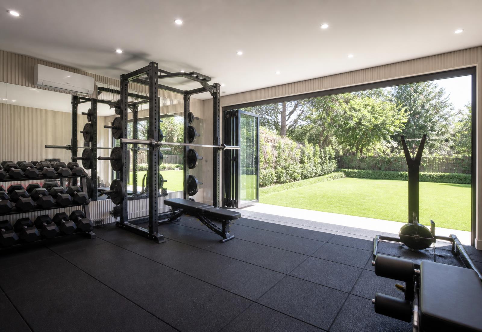 Garden gym with rubber flooring, squat rack and bi-fold doors opening onto a lawn
